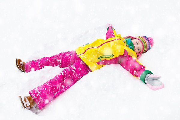 Ett barn i färgglada vinterkläder som ligger i snön och gör en snöängel medan det snöar.